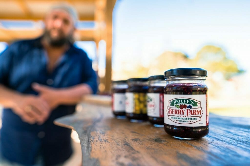 A man standing in front of jars of jam, showcasing the latest label printing by Hobart's Wolfe Brothers. Noble Ink